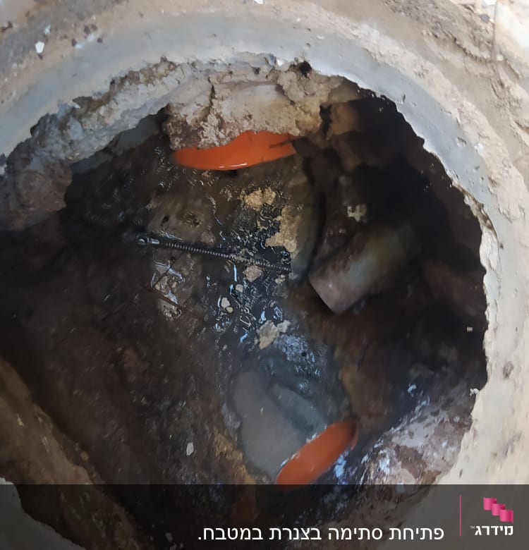 פתח ביוב עם צינור כתום וחלקי מתכת